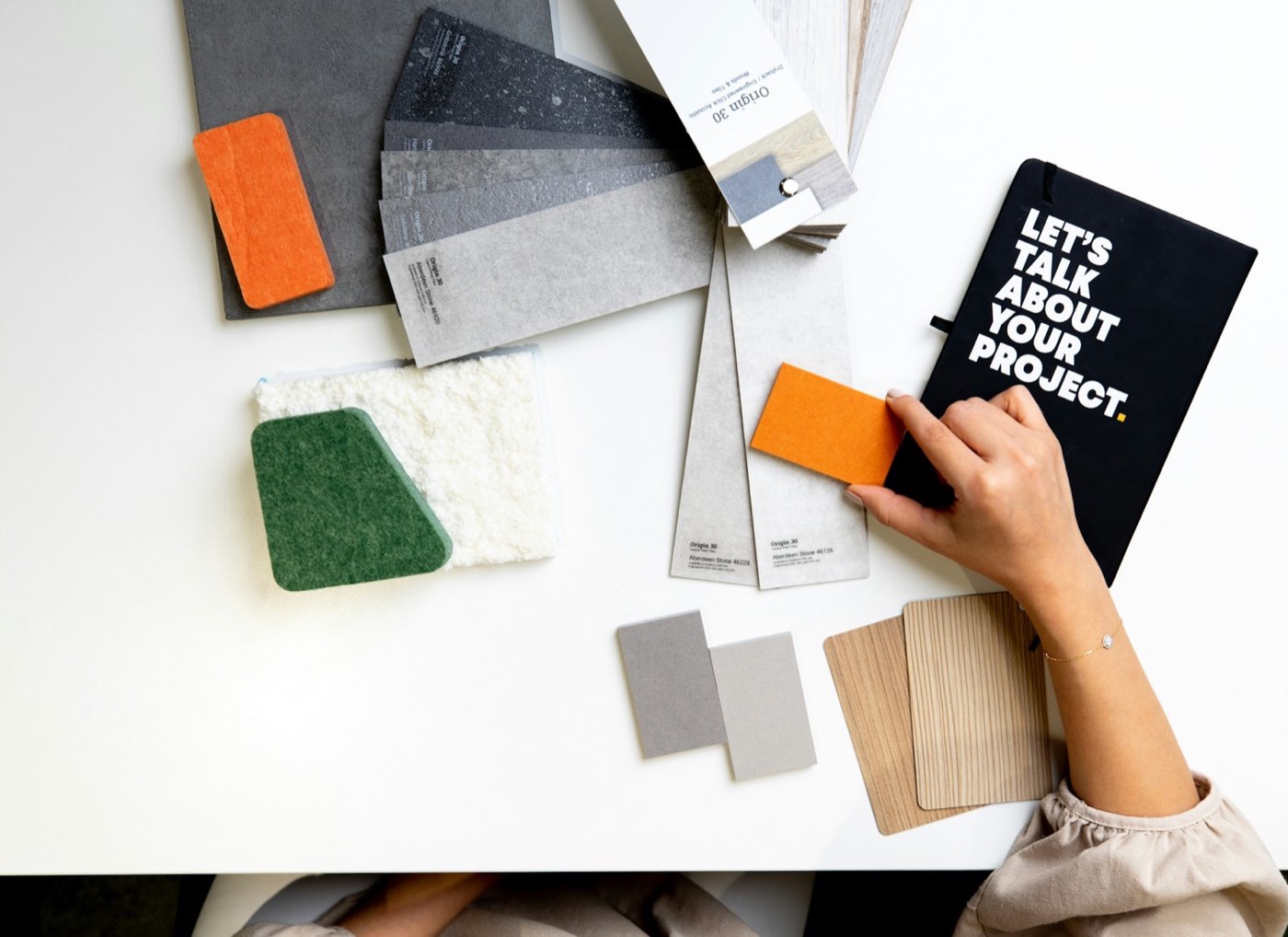 Hands sorting fabric swatches and color cards on a white desk