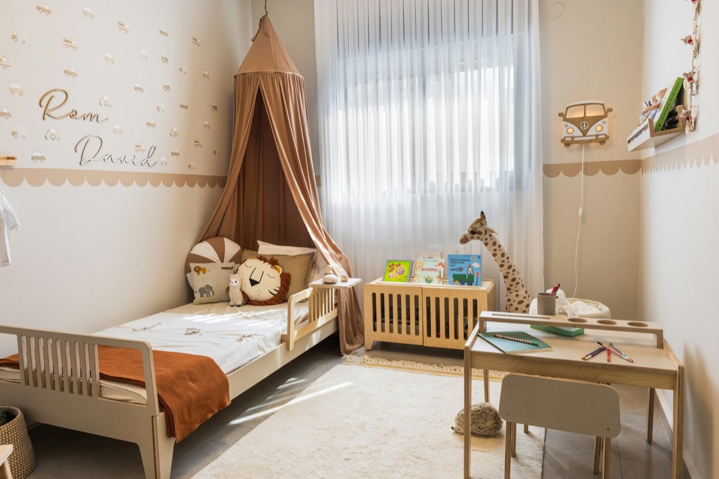 A child&rsquo;s room with a low wooden bed under a fabric canopy and soft daylight