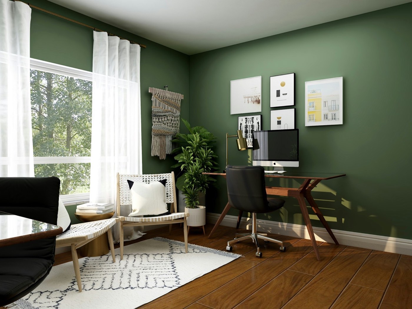 A home office with a green wall, framed prints, a wooden desk and a window onto trees